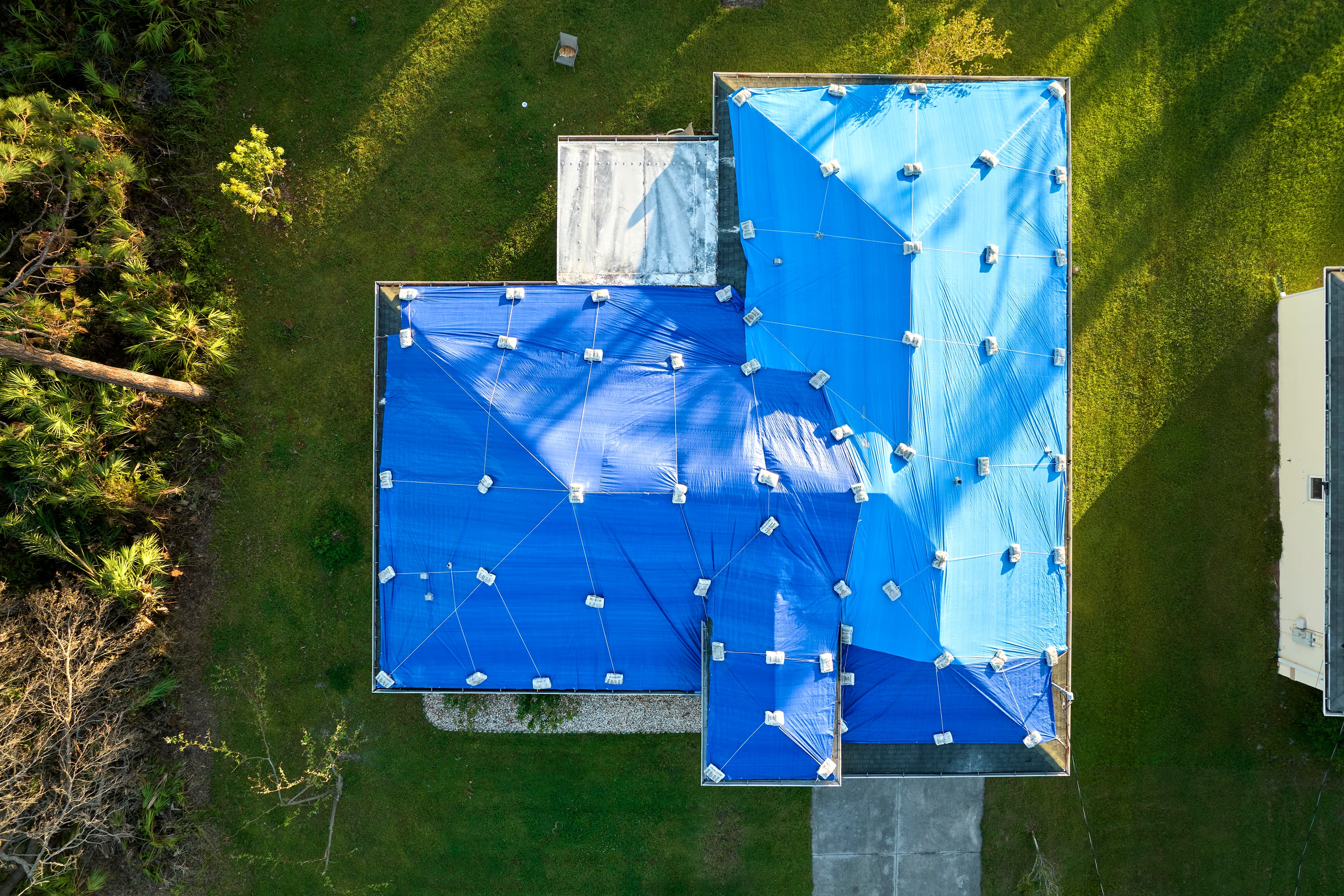 Blue emergency tarp covering active storm damage on a residential roof.